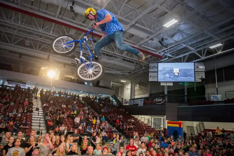 BMX rider performing a stunt in air basketball arena with innovox loudspeakers hanging